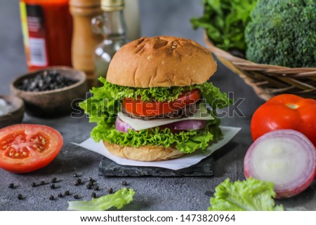 Photo of fresh burger on wooden cutting board on dark background.
Homemade hamburger with beef, onion, tomato, lettuce and cheese. Homemade fast food. Dark textured background. Copy space. Image
