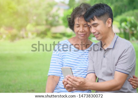 Middle-aged Asian mother and son Looking at a smartphone with a smile and being happy at the park Is an impressive warmth