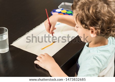 Child painting with watercolors on paper. Concepts back to school and childhood.