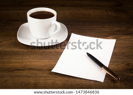 A cup of coffee, a white piece of paper with a pen on the desk top
