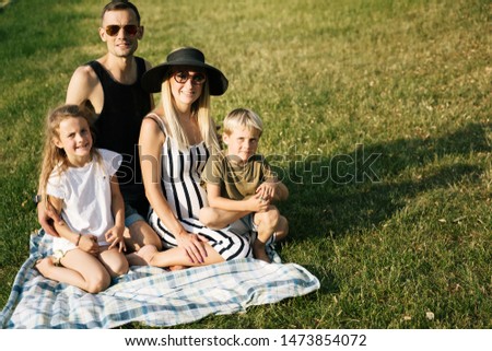 Picture of happy parents with son and daughter sitting on plaid on picnic on summer day