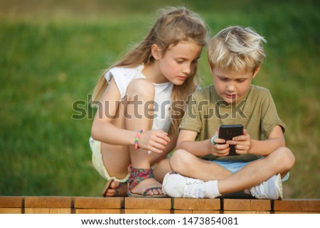 Picture of boy and girl with telephones hands sitting on wooden fence outdoors