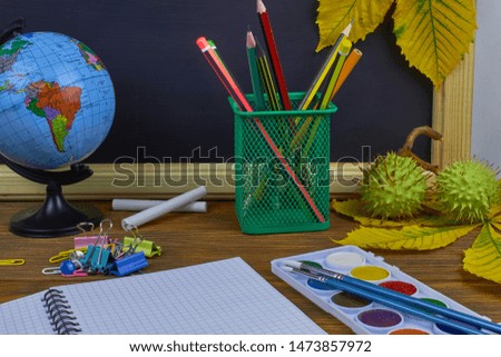 Back to school concept. School supplies on a wooden table on a blackboard background with yellow chestnut leaves