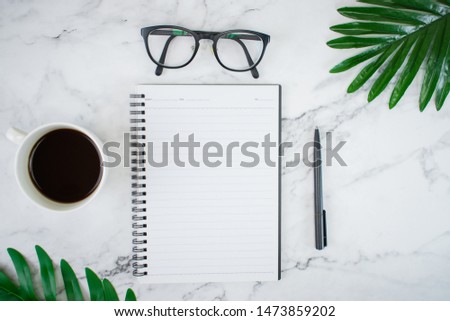 The image of workspace with notebooks and accessories, with palm leaves on the table, white marble pattern.