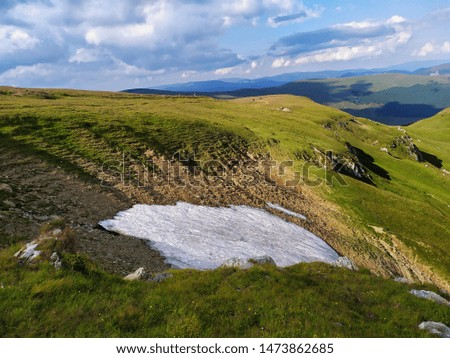beautiful mountain view with unpaved snow on a summer day. Beautiful sky with clouds. Image from the top of a mountain. Mountain, sun, green and a piece of snow. 