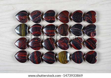 Twenty-four red and iron tiger eye heart-shaped stones are stowed four rows. Six pieces in each one. Top view.