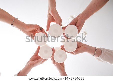 Bridesmaids, holding white glasses with champagne, in cheers process. Close-up picture from below, of young women's hands with goblets at bridal shower henparty bachelorette party, drinking wine