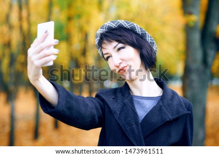 Beautiful woman taking selfie by smartphone and having fun in autumn city park, fall season, yellow leaves