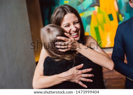 Fashion happy brown hair surprised excited painter woman or girl with pigtail laughing smile hugging with friend on celebration exhibition opening party  in art gallery with friends and paint on back Royalty-Free Stock Photo #1473999404