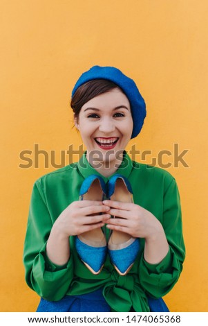 The concept of fashionable summer, blue and green colors. Stylish woman in a blue beret and a green shirt is standing against the orange wall with blue shoes and various emotions close