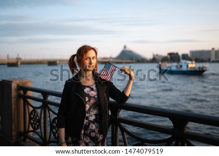 Redhead woman holding American Flag portrait in the sunset by the river - Traveler and explorer