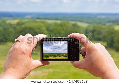 A woman using the rear lcd screen to compose and take a landscape photo with her compact digital camera using liveview.