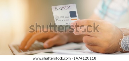 close up of platinum credit card in hand with background of blured laptop keyboard