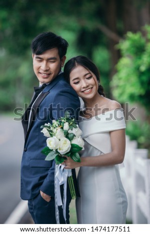 Wedding photo outdoor, Young couples are embracing happily with a green grass background. The bride and groom are excited and delighted.