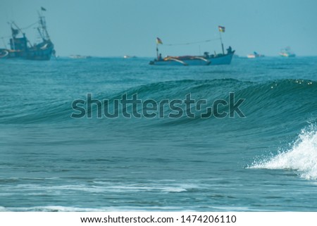 Close up of sea waves with defocused fishing boats in the background. Morning outdoor picture of ocean high tide waters in summer, tropical beach vacation destination. Colva, Goa, India