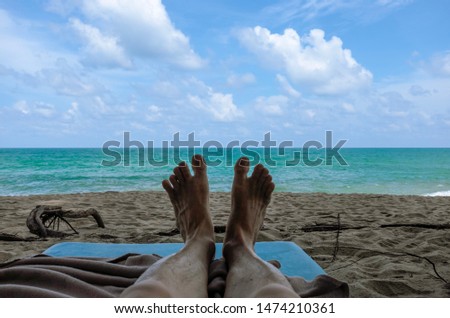 Picture of both legs and ocean back ground while lying down on a shaded beach in monsoon season. Vacation. Resting.