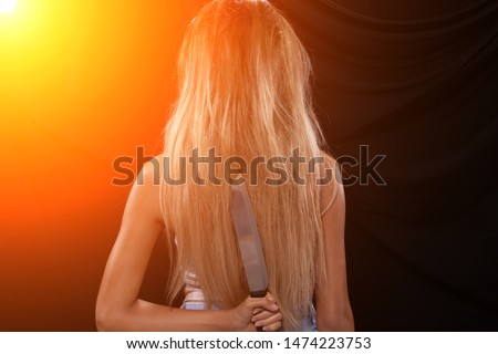 Back side view of Asian Woman long dyed blonde hair hold Kitchen sharp Knife in hand, studio lighting black backgrounds, ready to betray by stabbing
