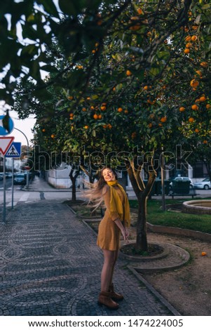 girl in a dress on the sidewalk waving her hair. trees with oranges on city street.