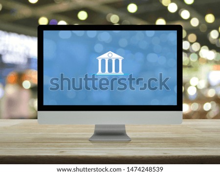 Bank flat icon on desktop modern computer monitor screen on wooden table over blur light and shadow of shopping mall, Business banking online concept