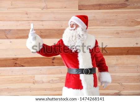 Portrait of Santa Claus taking selfie on wooden background