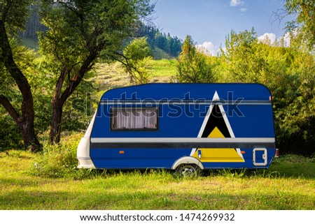 A car trailer, a motor home, painted in the national flag of  Saint lucia stands parked in a mountainous. The concept of road transport, trade, export and import between countries. Travel by car