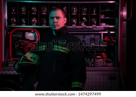 Portrait of young fireman looking to camera with helmet in hand near fire truck