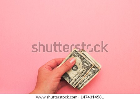 Female hand with a neutral manicure holding money dollar bills on pink background. Strategy and business concept