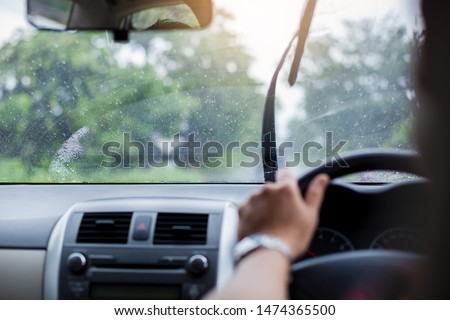 Selective focus to man driving a car with rain droplet on windshield and wiper. Windshield wipers from inside of car, season rain.