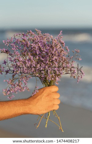 male hand giving bouquet of wildflowers on the sea beach background