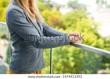 Female Business Leader With Arms Crossed. Beautiful young woman in smart casual wear keeping arms crossed standing against green background. Home broker standing on the taras of modern property.