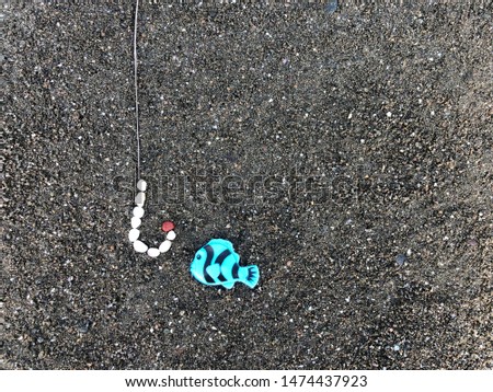 Fish near the fishing hook. In the sand, a fish is depicted, next to it is a fishing hook. Concept: Temptation, Bait