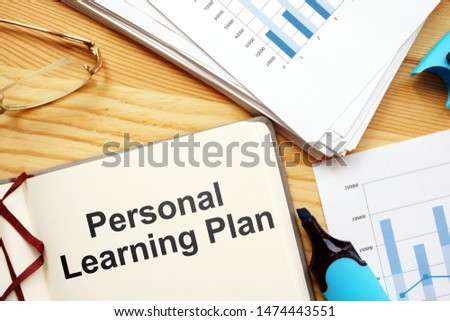 Text sign showing Personal Learning Plan. The text is written on a paper of notebook. Papers with graphs and colored papers, pen, wooden background are on the photo too.