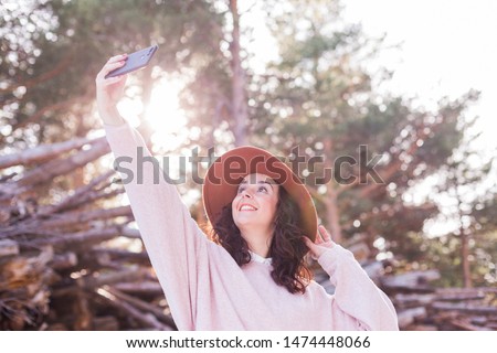 young beautiful woman in the woods taking a picture with mobile phone. Back light. Outdoors and lifestyle