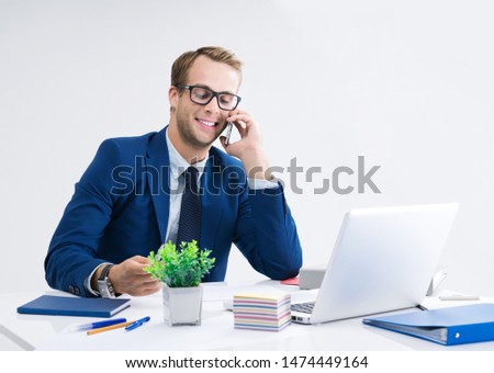 Businessman in glasses and blue suit working with cellphone and laptop computer at office. Success in business, job and education concept.
