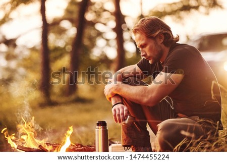 Enjoying the break. Man in black shirt near the campfire in the forest at his weekend time.