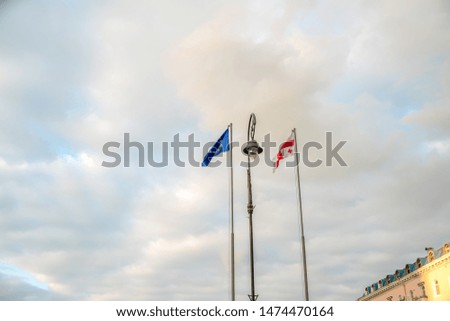 The flag of Georgia and the flag of the European Union against the sky with clouds, between them a lamppost