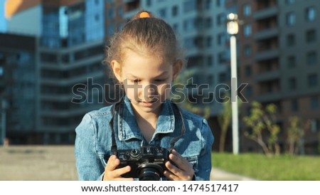 Portrait of a little girl holding a camera in her hands. She takes pictures and smiles, looks at the camera.