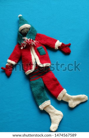 Top view of Santa clothes with accessories as gloves, hat, scarf, socks in white, red and green knit from yarn on blue background, small decorations for Christmas season at winter holiday