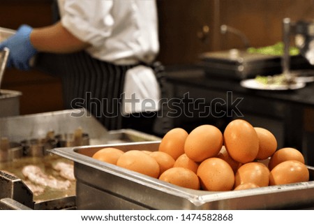 Close-up pictures of chicken eggs in a rectangular stainless steel container with a back blurred image of the chef who is cooking.