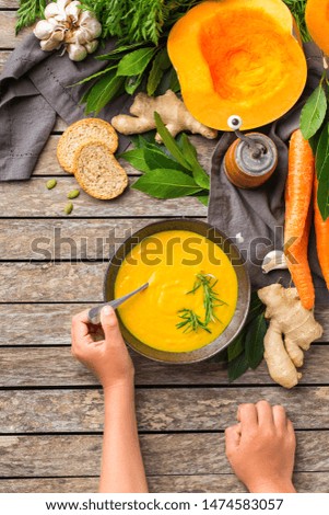 Healthy food, clean eating concept. Seasonal spicy fall vegetables creamy pumpkin and carrot soup with ingredients on a rustic wooden table. Top view flat lay background with kid child hands