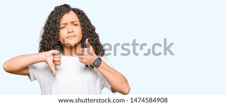 Young beautiful woman with curly hair wearing white t-shirt Doing thumbs up and down, disagreement and agreement expression. Crazy conflict