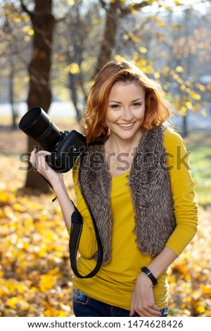 Young pretty woman in the park with photocamera in the autumn day