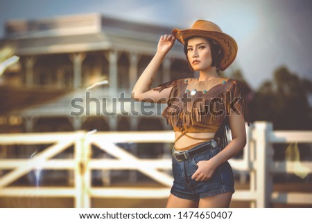 Asian girl in a cowgirl outfit standing at the farm fence.
