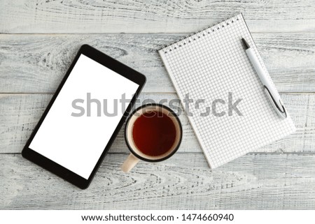 black electronic tablet,paper notebook and a Cup of tea or coffee on a vintage shabby white wooden background. the view from the top. flat lay