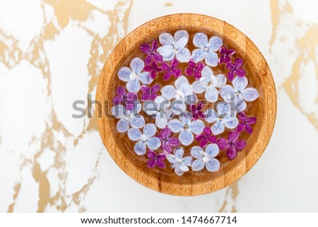 Floating lilac flowers in a bowl of water on marble background with copyspace for text. Top view