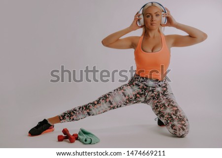 Portrait of caucasian pretty woman listening to music using wireless headphones in studio after workout isolated over gray background