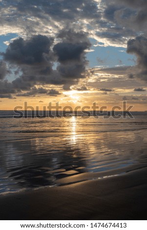 dramatic Sunset  with Relections on a sandy beach in shades of orange and blue with space for copy