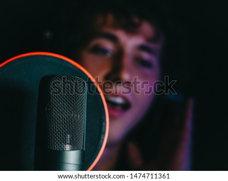 Young handsome singer man emotionally writing song in the studio. Recording new melody or album. Male vocal artist with curly hair singing alone. 