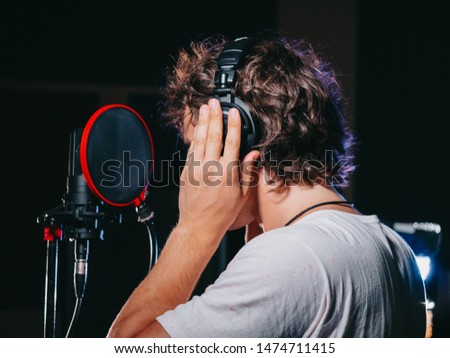 Young handsome singer man puts on headphones in the studio. Recording new melody or album. Male vocal artist with curly hair preparing for working. 
