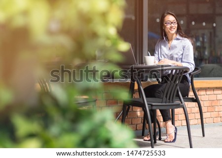 Portrait of a young asian freelancer in glasses looking aside while sitting in the cafe with a laptop and listening to podcasts. Horizontal shot. Selective focus.